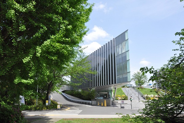 A sleek, modern glass building at the Tokyo Institute of Technology, surrounded by lush greenery and a clear blue sky.