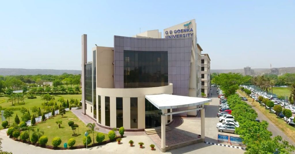 Front view of GD Goenka University’s modern campus building surrounded by greenery and parked cars.