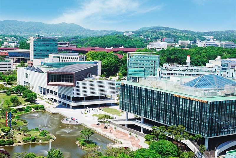 A panoramic view of Korea University’s campus featuring modern buildings, a landscaped pond, and surrounding green hills.